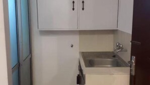 A compact kitchen with a sink, cabinets, and a trash bin. - Stay.Plus 2 Bedroom Shree Apartment (Mombasa)
