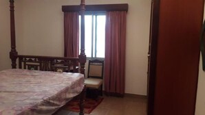 A bedroom with a four-poster bed, a chair, a window with curtains, and a door. - Stay.Plus 2 Bedroom Shree Apartment (Mombasa)