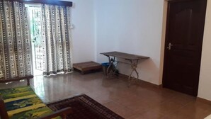 A room with a bed, a small table, a door, and patterned curtains. - Stay.Plus 2 Bedroom Shree Apartment (Mombasa)