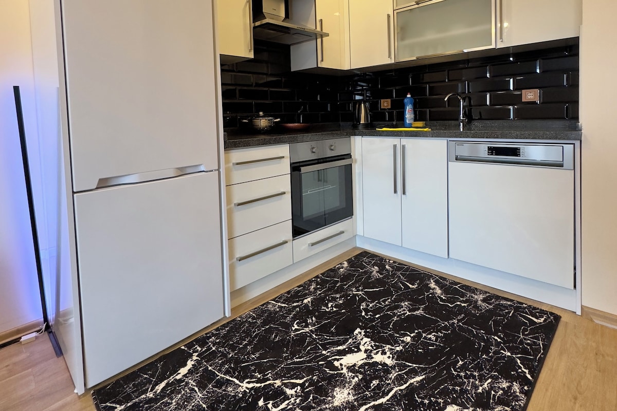 Una cucina moderna con mobili bianchi, un tappeto con motivo marmorizzato nero e un forno a incasso.