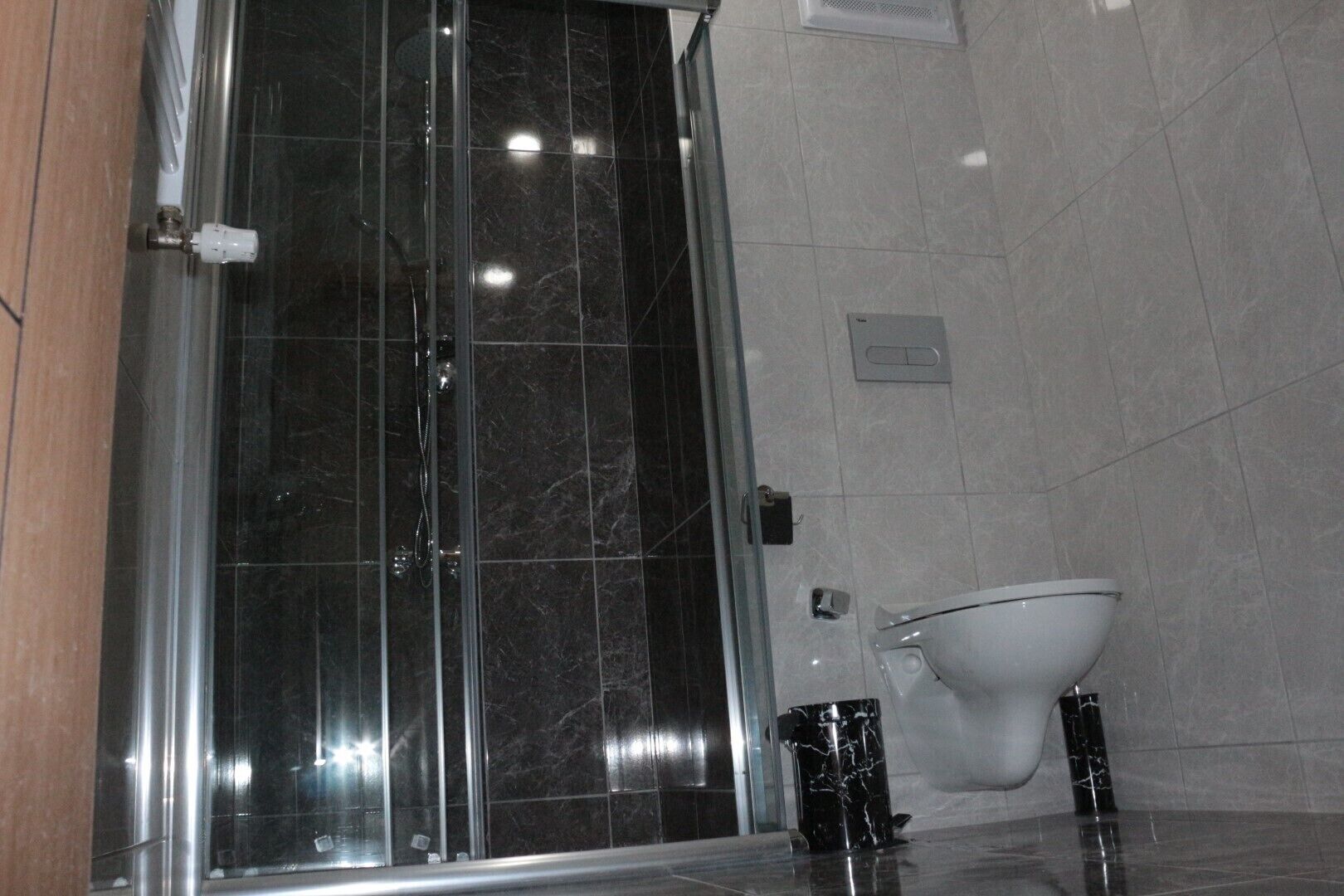 Een moderne badkamer met een glazen douchecabine, een wit toilet en een vloer van marmer.