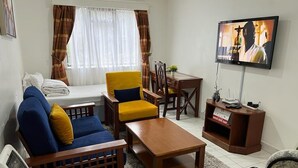 Un salon comprenant un canapé, un fauteuil, une table basse, un téléviseur et une petite table à manger.
