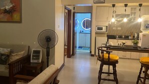 Une cuisine moderne équipée d’un four à micro-ondes, d’un évier et de tabourets en bois. Un ventilateur se trouve à gauche, et un panneau encadré accroché au mur porte l’inscription : « On n’est jamais si bien que chez soi ».