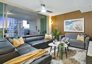 Ein modernes Wohnzimmer mit einer schwarzen Ledersofa, einem grauen Sessel und einem kleinen Couchtisch. Es gibt ein großes Fenster mit Blick auf eine Stadtansicht und einen Balkon.