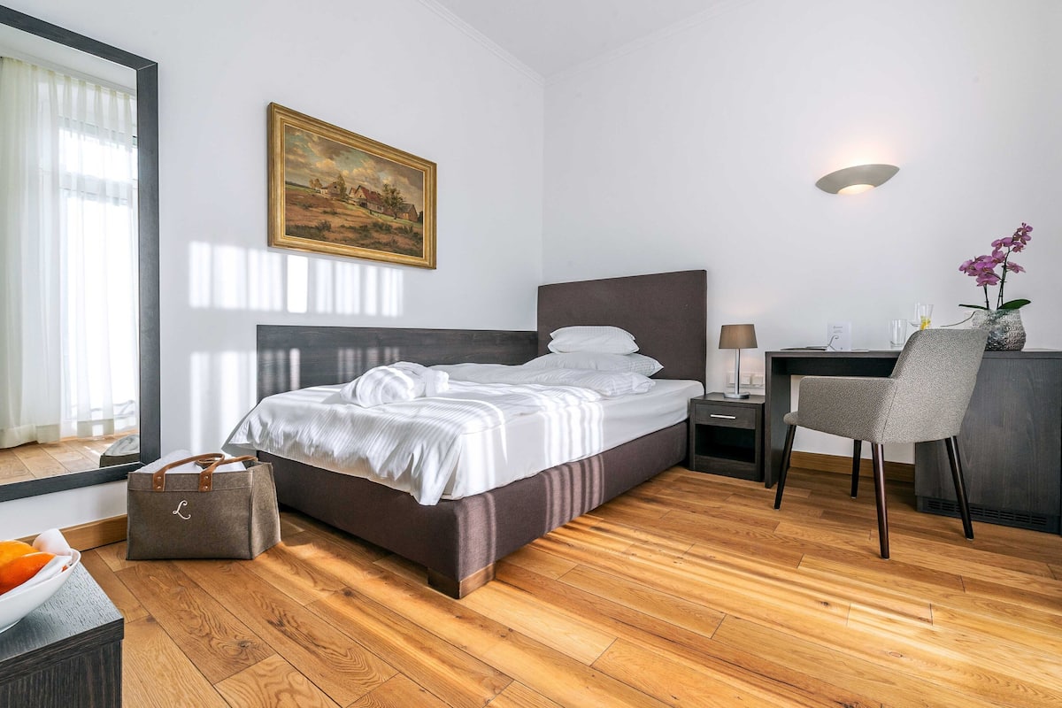 Un dormitorio ordenado con cama, mesita de noche, silla y escritorio.