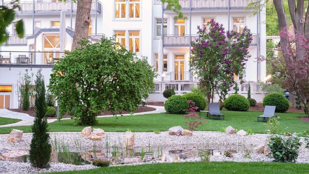 Un hôtel à plusieurs étages doté d’un jardin bien entretenu, comprenant un étang, divers arbustes et des espaces aménagés pour se détendre.