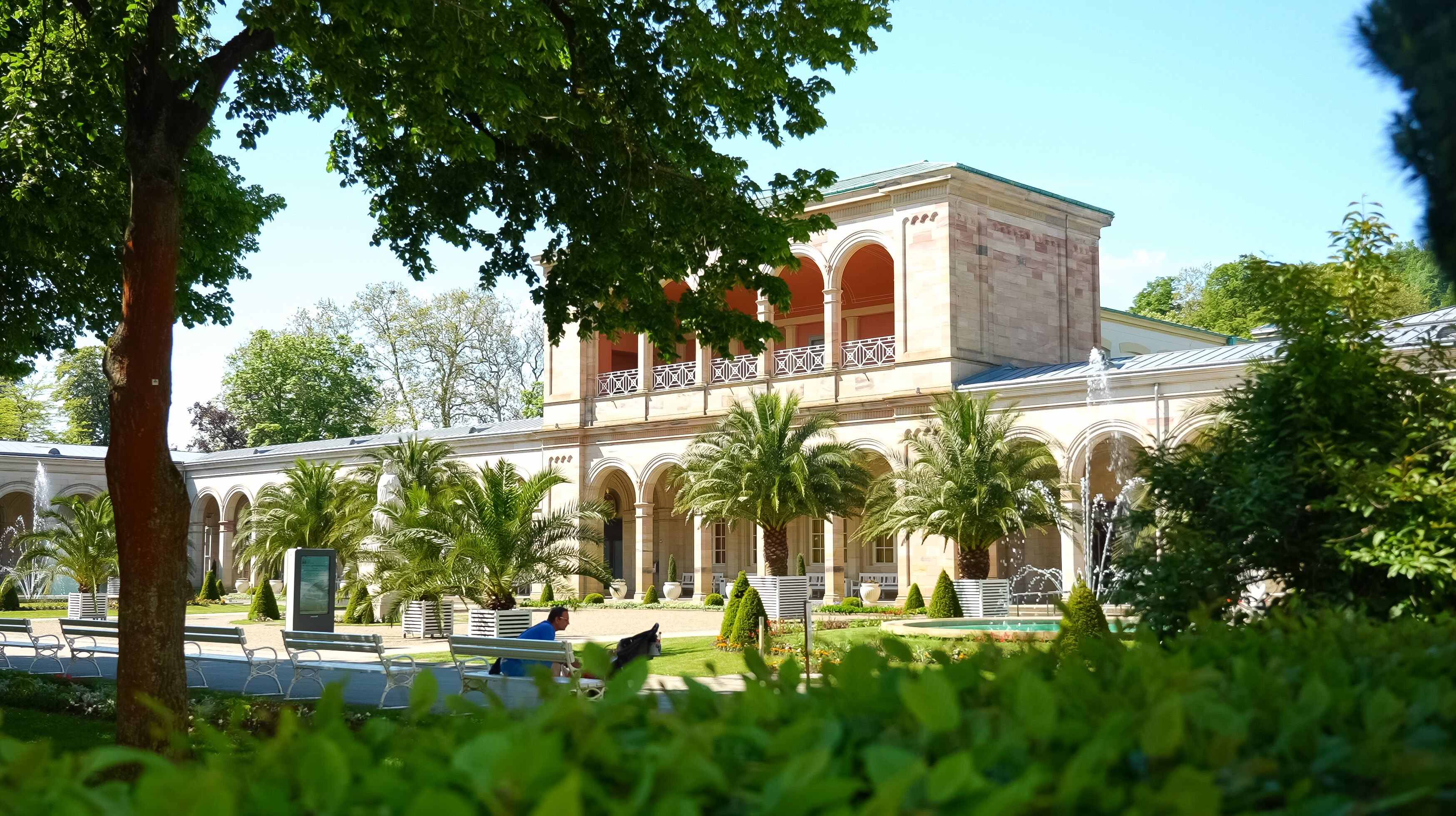 Un edificio de estilo arquitectónico clásico, con un patio central con palmeras y bancos.