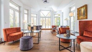 Une pièce spacieuse dotée de grandes fenêtres, d’un ventilateur de plafond et de différents types de sièges, notamment des canapés et des tables.