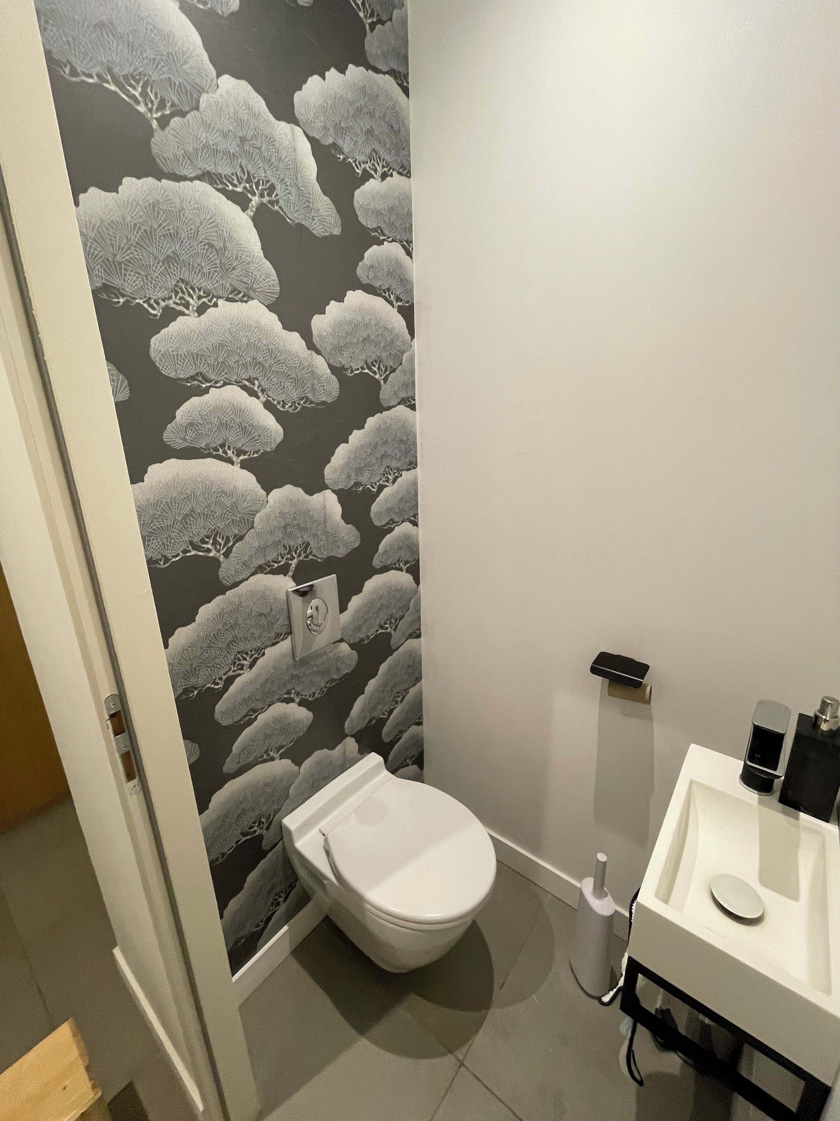 A bathroom with a toilet, sink, and a wall with a tree pattern.