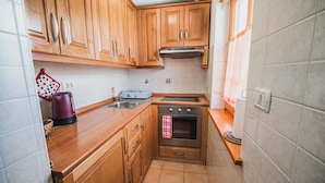 Eine kleine Küche mit Holdekor-Schränken, einem Edelstahlbackofen und einer gefliesten Spritzschutzwand.