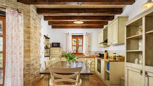 A rustic kitchen with stone walls, wooden beams, and a dining table with chairs.