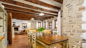 A rustic dining area with a wooden table and chairs, a potted plant, and a stone wall.
