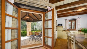 An open door leading to an outdoor patio with a stone table and chairs, a kitchen area with a wooden countertop and cabinets, and a stone wall.