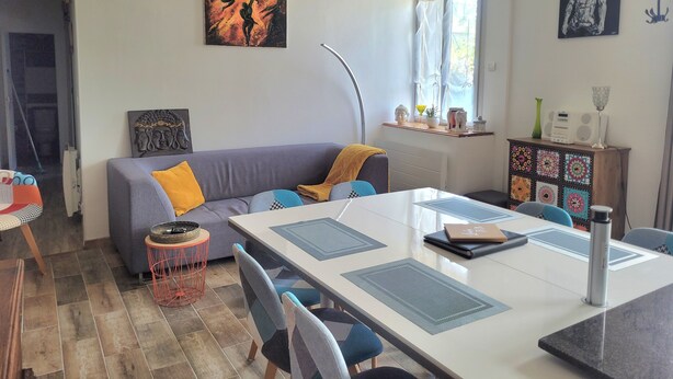 A modern living room with a grey sofa, a dining table with chairs, and artwork on the walls.