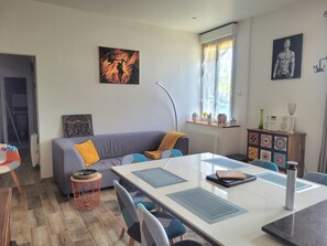 Un salon moderne avec un canapé gris, une table à manger et des chaises, ainsi que des œuvres d’art accrochées aux murs.