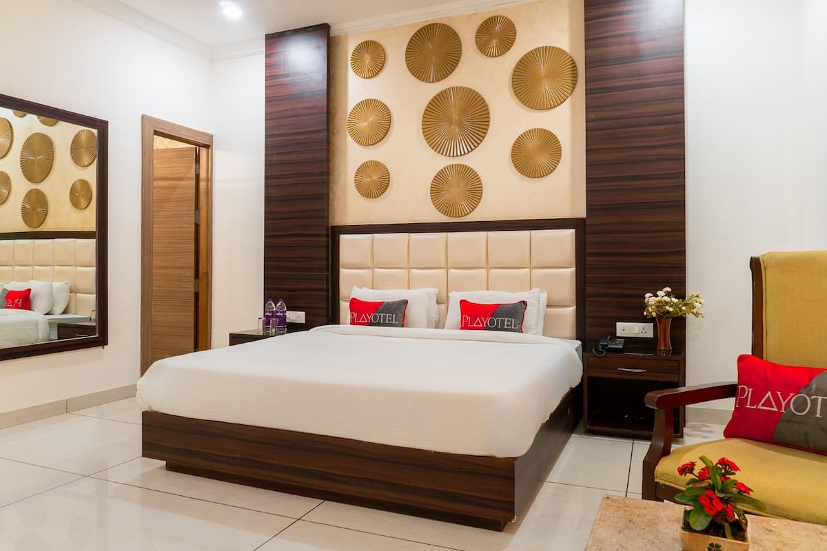 A hotel room with a large bed, a nightstand, a chair, a mirror, and decorative wall panels.