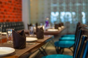 A restaurant setting with tables set for dining, chairs, and a glass of water on the table. - Playotel Resort Bhopal (Bhopal)