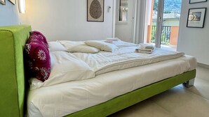 A bedroom with a green bed, white bedding, a hanging light fixture, and a door leading to a balcony.