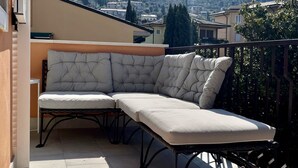 A balcony with a cushioned seating area and a view of a hillside town.