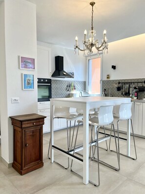 Eine moderne Küche mit einer zentralen Kochinsel, weißen Barhocker, einer Chandelüster und einem Holzkasten.
