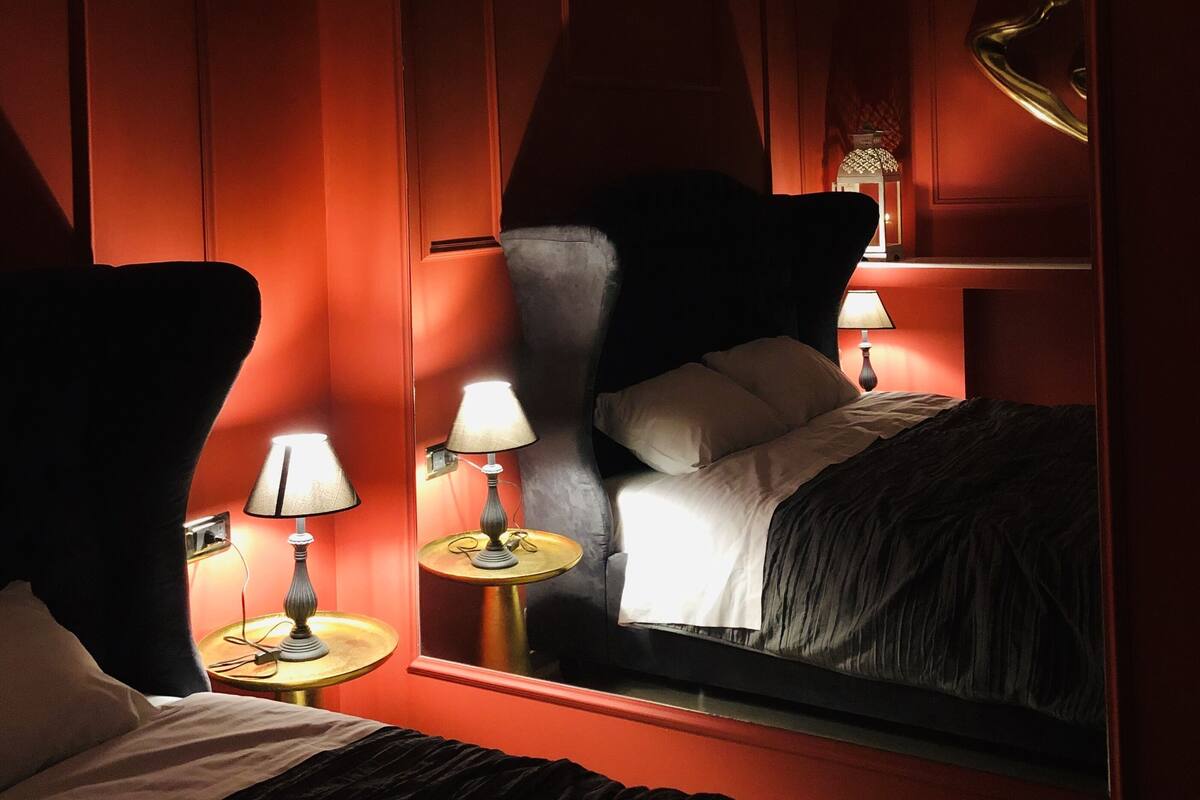 A hotel room with a large mirror reflecting the bed and a lamp on a bedside table.