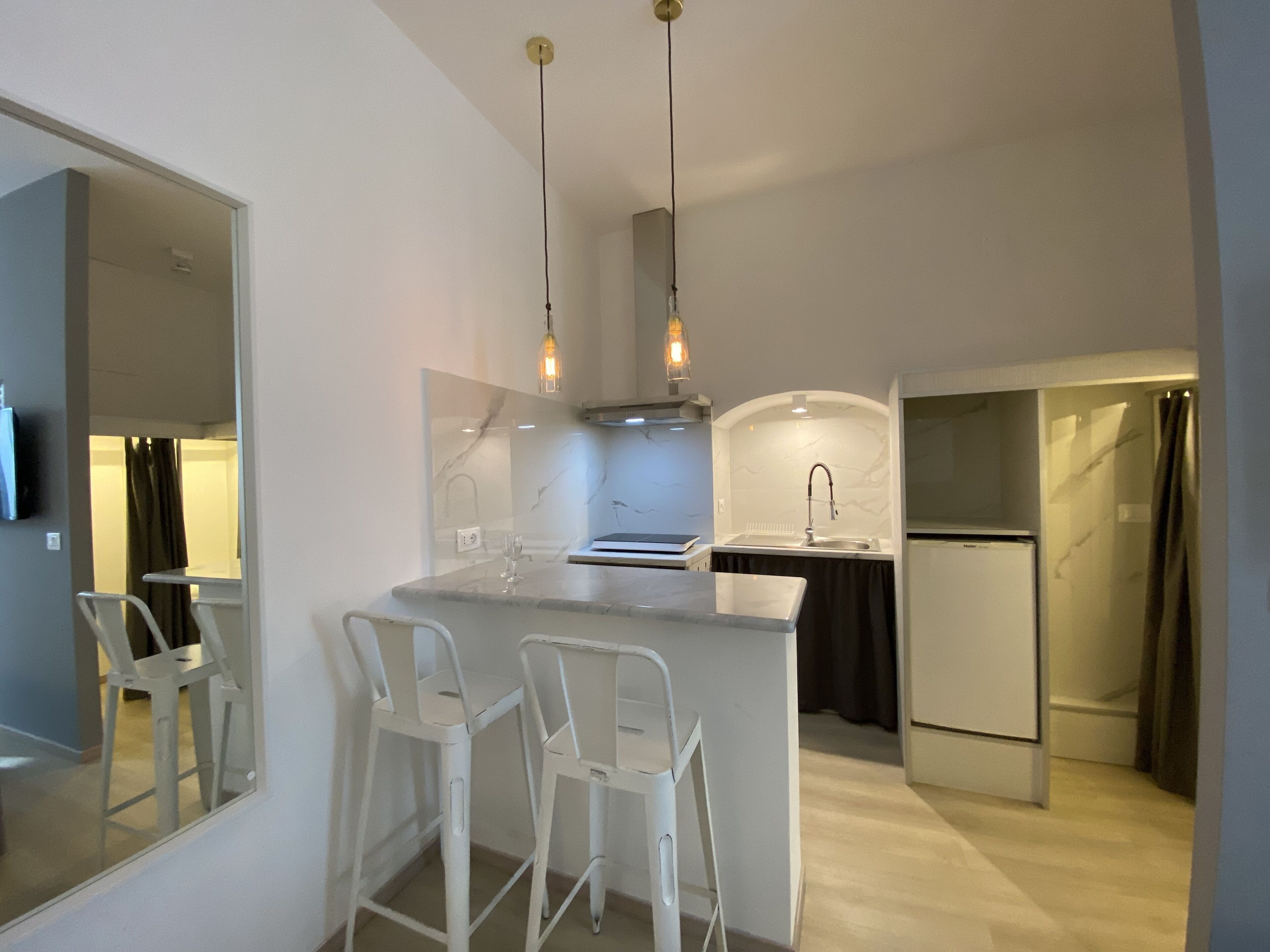 Une cuisine moderne dotée d’un plan de travail en marbre, de tabourets de bar blancs et de luminaires suspendus.