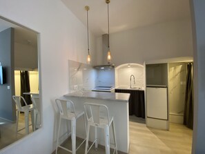 Cozinha moderna com bancada de mármore, banquetas brancas e iluminação pendente.