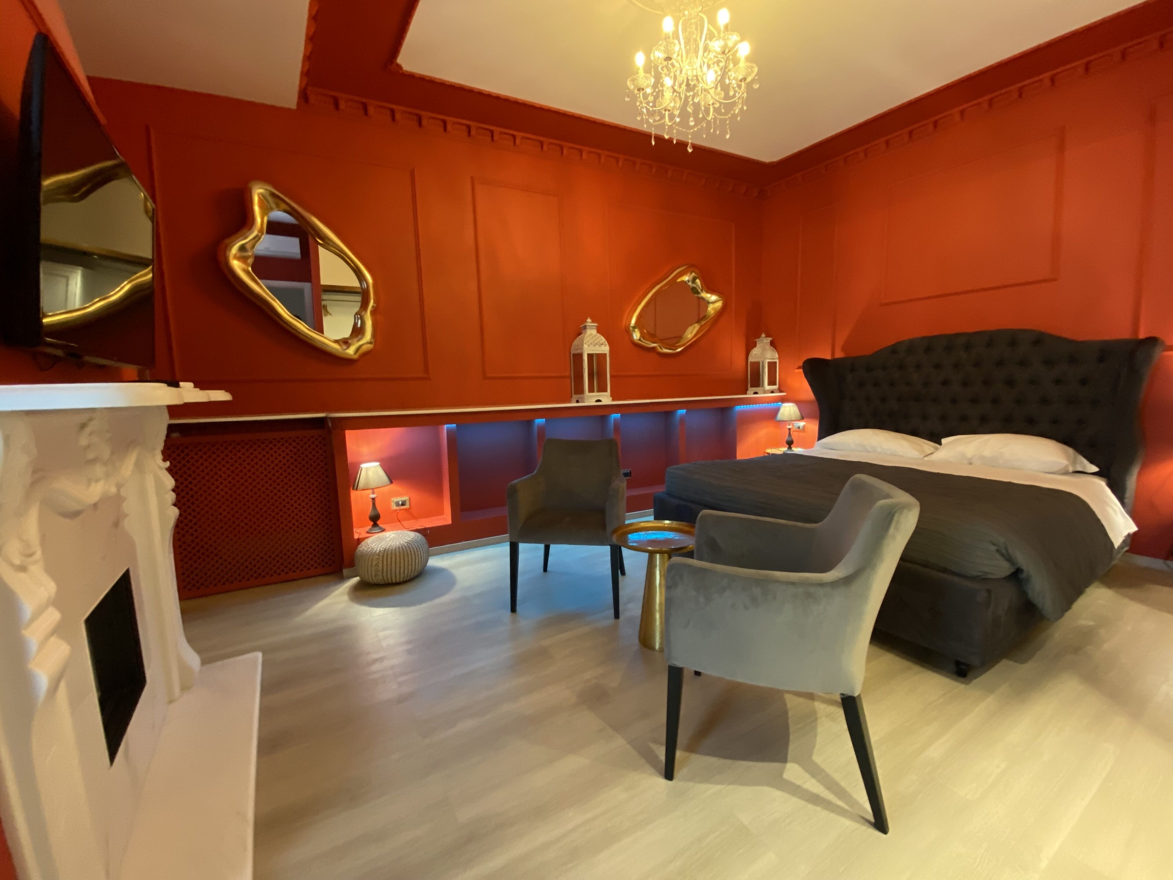 A modern bedroom with a large bed, a chandelier, a mirror, and a seating area with a chair and ottoman.