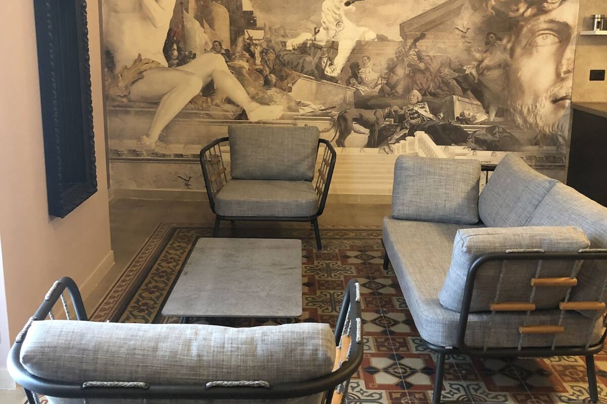 A room with a large mural, two armchairs, a sofa, and a patterned floor.