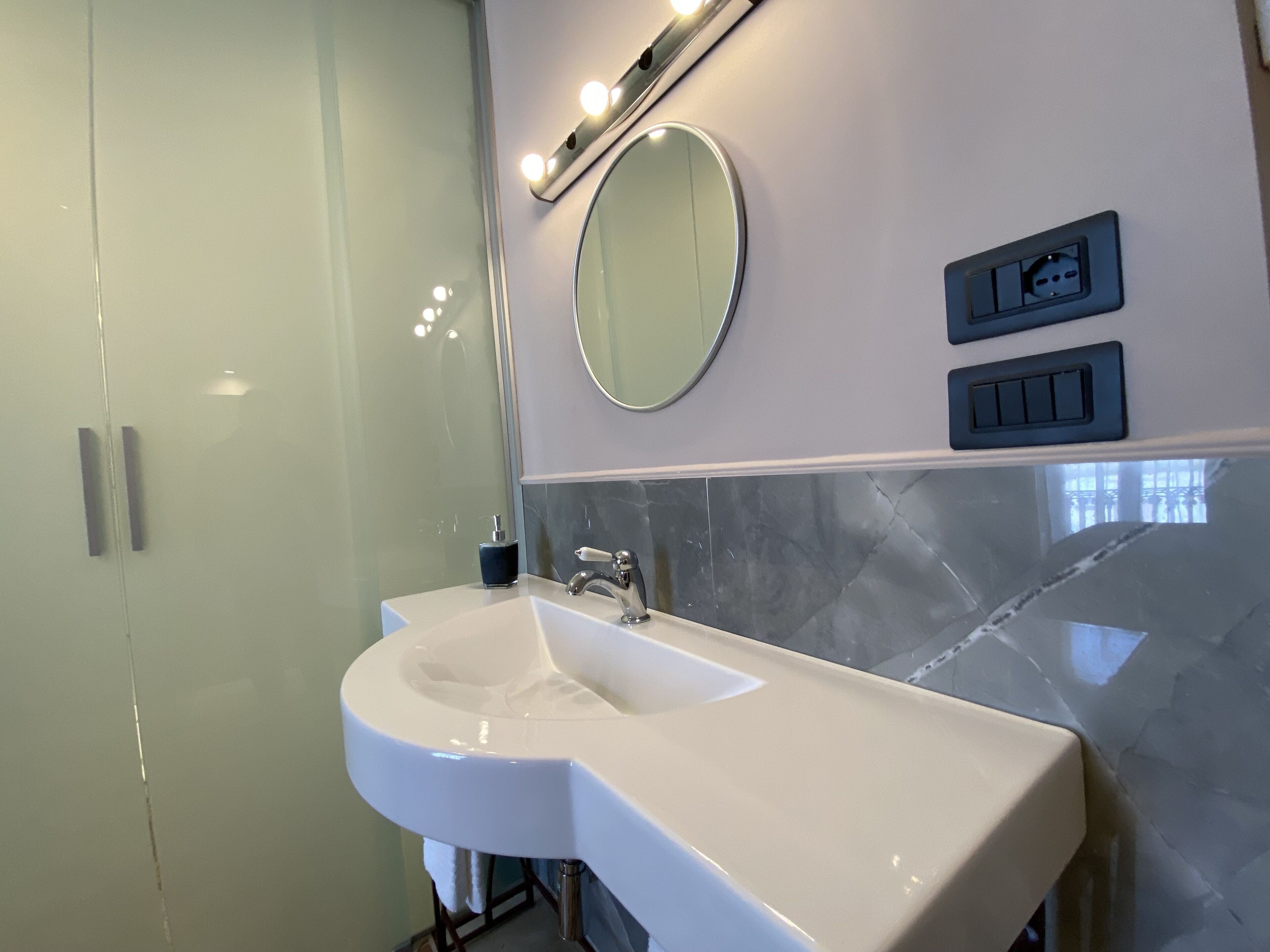 Une salle de bain moderne avec un lavabo blanc, un grand miroir et une douche à parois de verre.