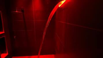 Un espacio de ducha con iluminación roja y un cabezal de ducha curvo.