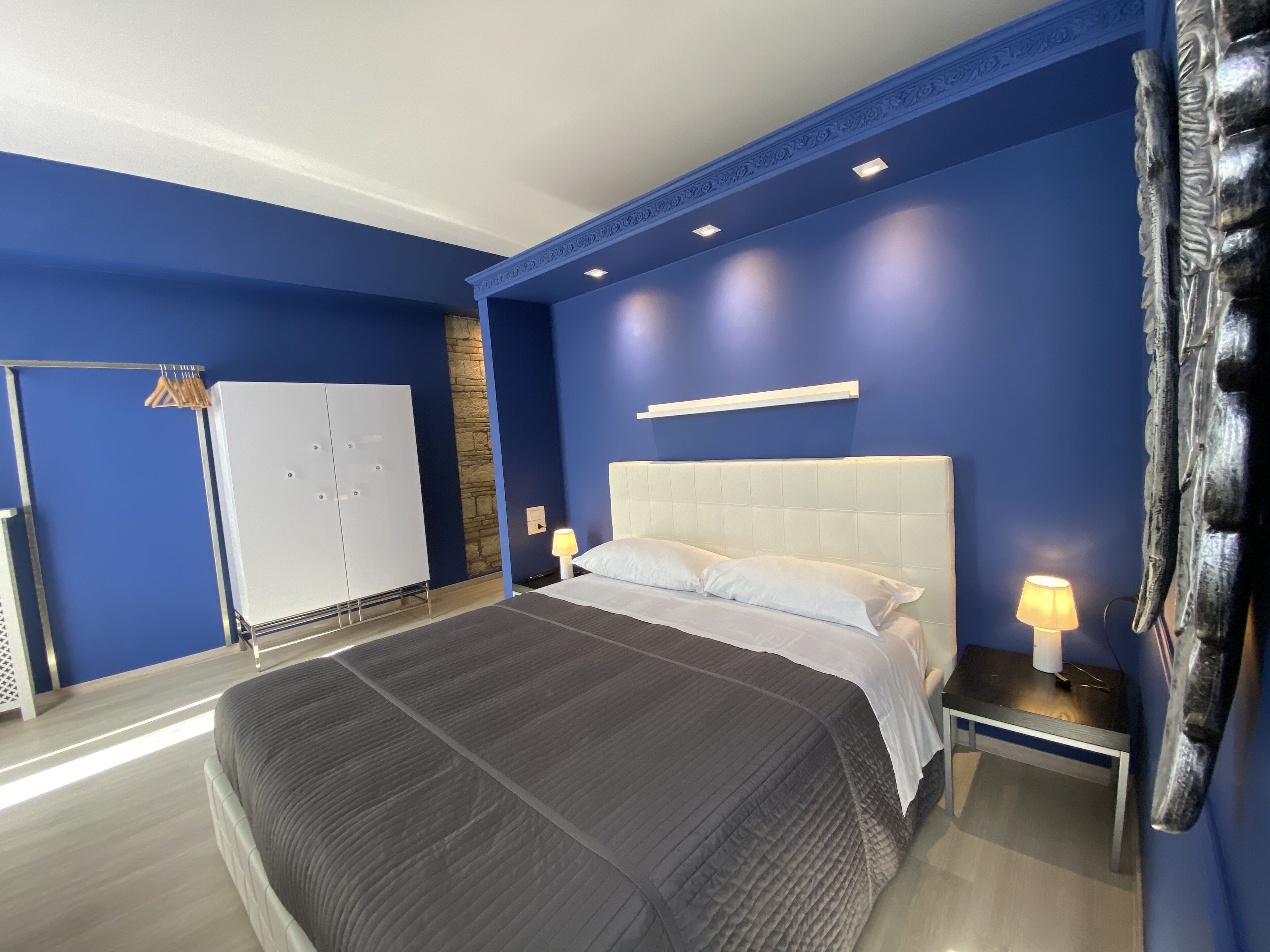 Een moderne slaapkamer met een groot bed, een kledingkast en een nachtkastje met een lamp.