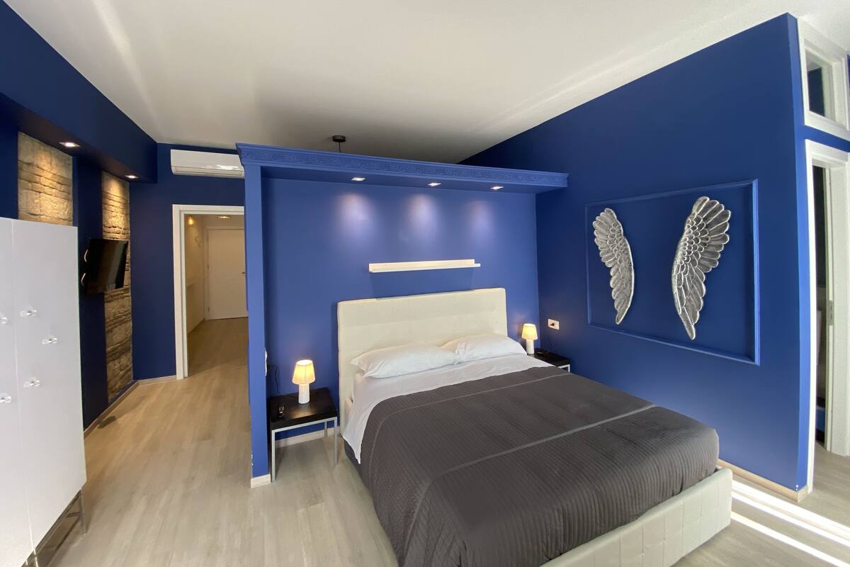 A modern bedroom with a large bed, a TV mounted on a brick wall, and a decorative wing on the wall.