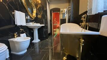 A bathroom with a black marble floor, a white pedestal sink, a gold-colored clawfoot bathtub, a white bidet, and a large mirror with gold fixtures.
