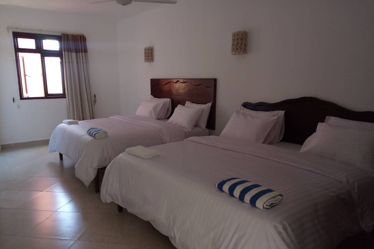 A hotel room with two beds, a window with curtains, a ceiling fan, and a wall-mounted artwork.