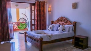 A bedroom with a wooden bed, a hanging chair, a small bedside table, and a view of the outside balcony. - Stay.Plus Shanzu Beachfront Apartment (Mombasa)