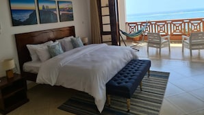 A bedroom with a bed, a nightstand, a bench, a hammock, and a balcony with a view of the ocean. - Stay.Plus Shanzu Beachfront Apartment (Mombasa)