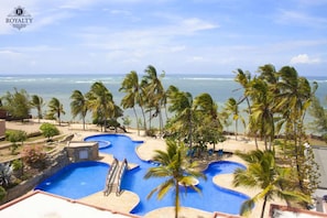 A resort with a pool area, palm trees, and a view of the ocean.