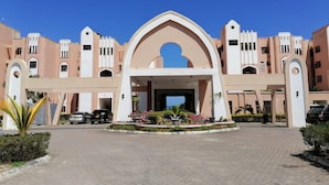 A hotel entrance with a central archway, paved driveway, and surrounding greenery. - Stay.Plus Shanzu Beachfront Apartment (Mombasa)