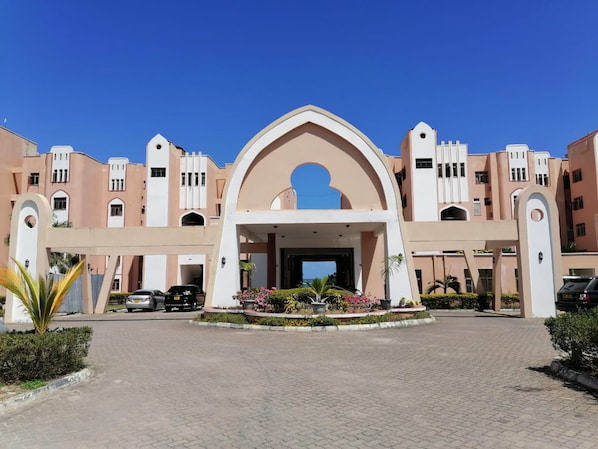 A hotel entrance with a central archway, paved driveway, and surrounding greenery.