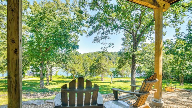 A wooden deck with Adirondack chairs and a small table, surrounded by trees and a view of a lake. - Reeds Spring Retreat w/ Lakeview Deck + Grill (Reeds Spring)