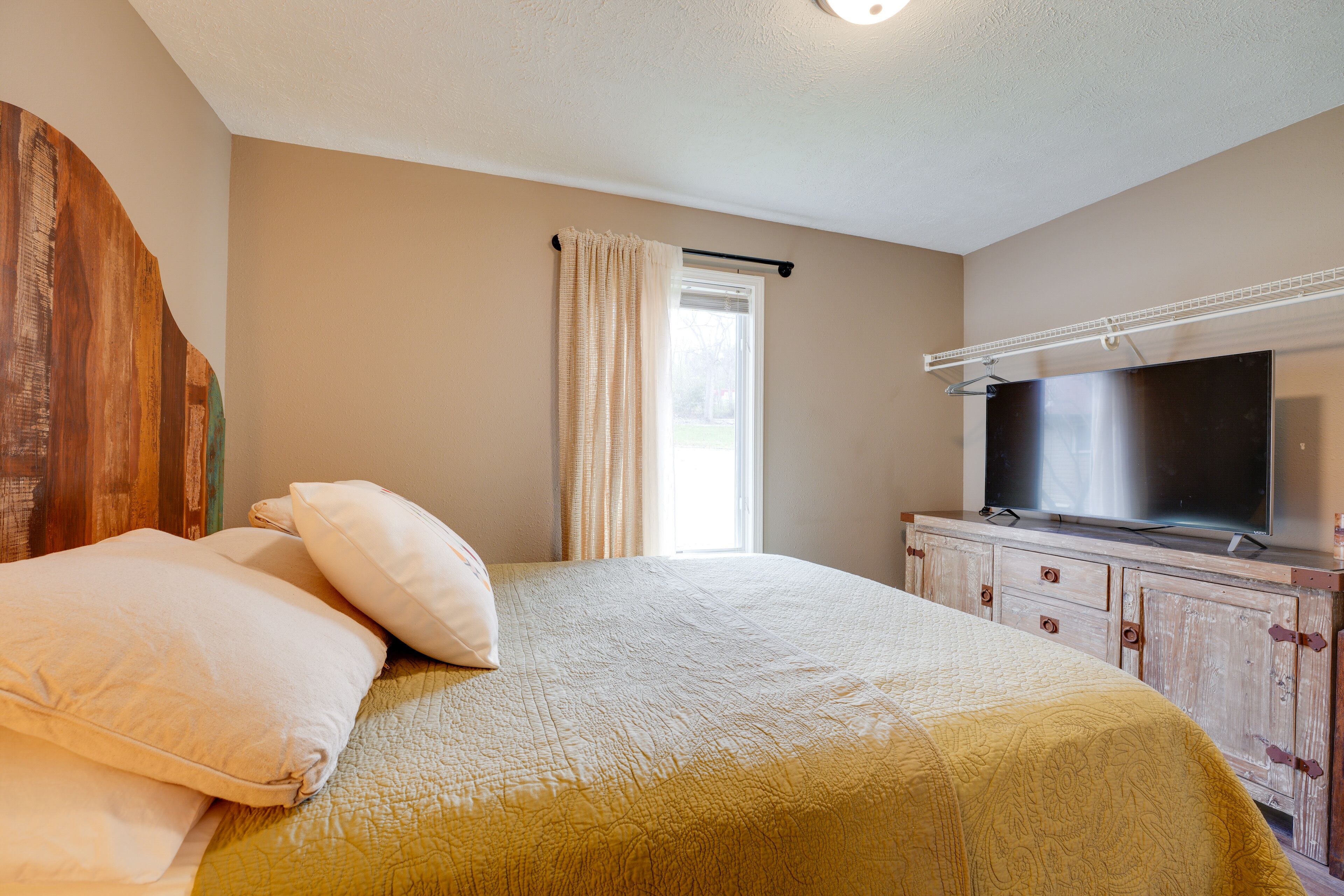 Ein Schlafzimmer mit Bett, Kissen, einem Fernseher und einem Fenster mit Vorhängen.