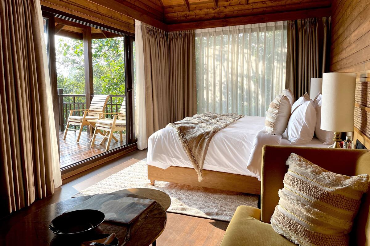 A wooden cabin bedroom with a bed, curtains, a table, and a chair.