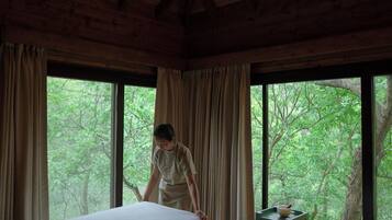 A room with two beds, large windows, and a view of trees.