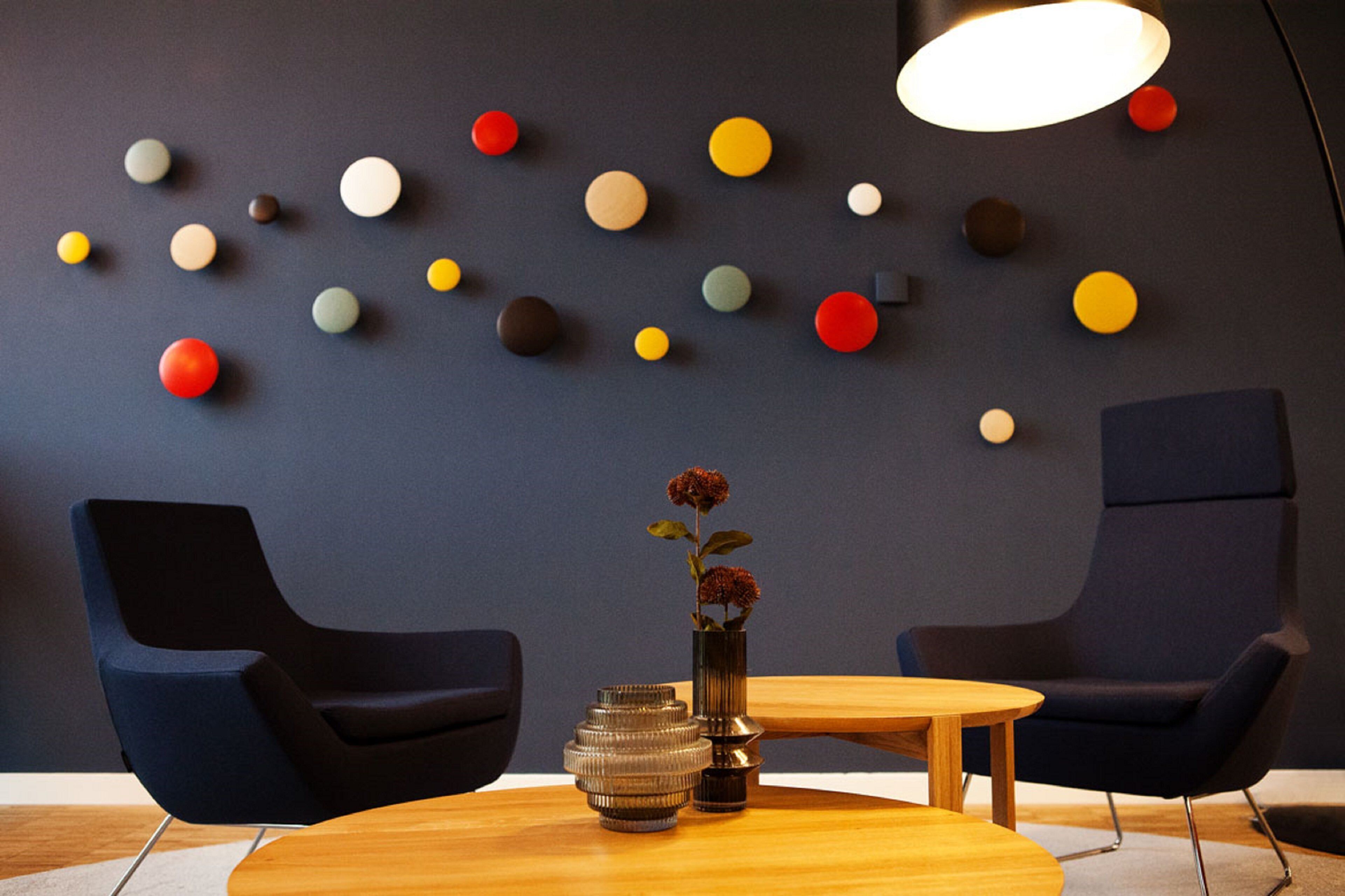 Een moderne kamer met twee donkerblauwe stoelen, een houten tafel en een wand versierd met meerkleurige bolvormige objecten.