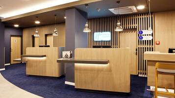 A hotel reception area with a modern design, featuring a reception desk, seating area, and a digital display.
