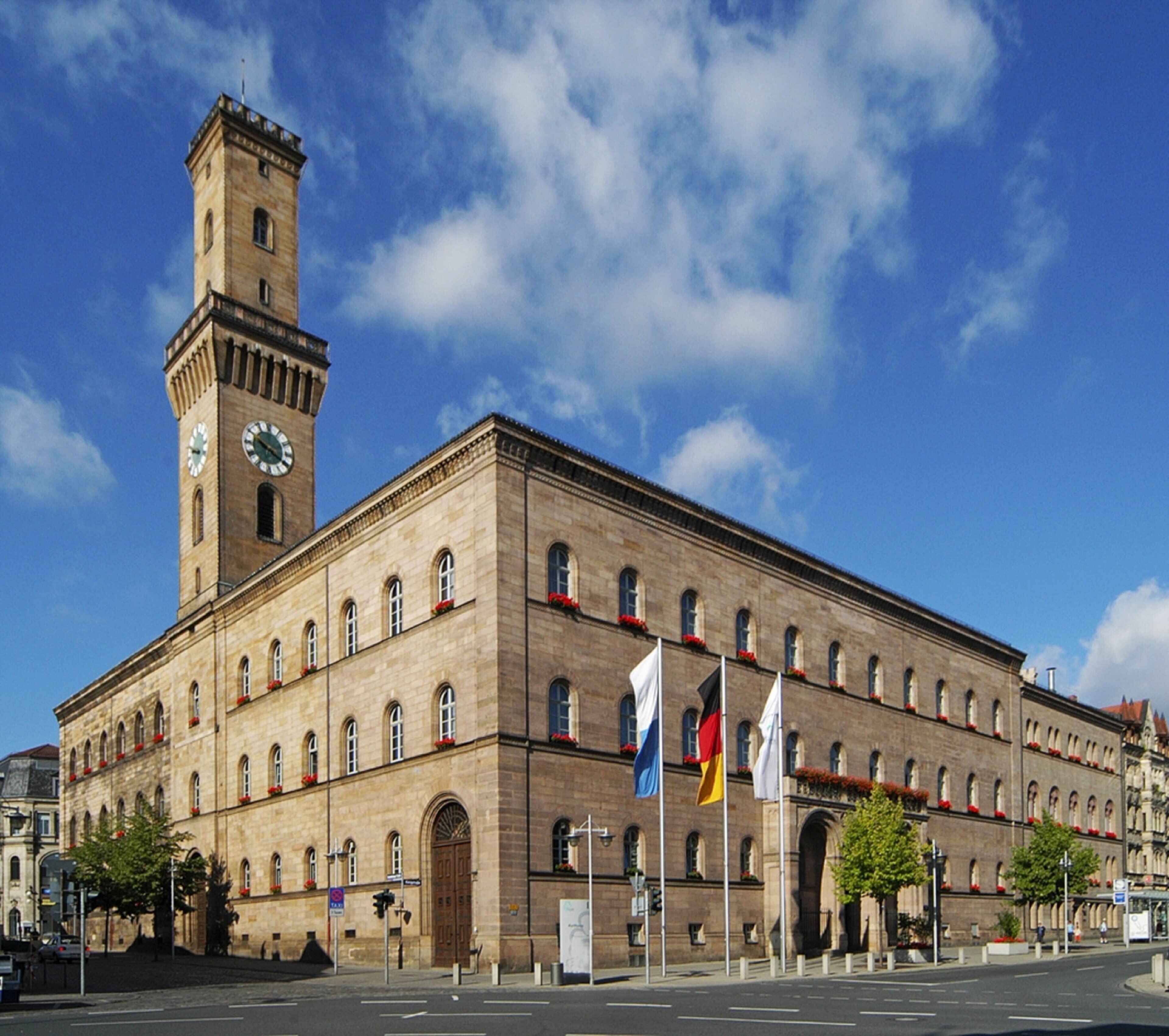 Un edificio grande e histórico con una torre de reloj, varias banderas y una entrada destacada.