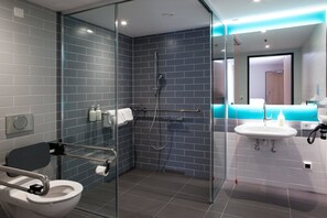 A modern bathroom with a glass-enclosed shower, a white sink, and a toilet with a safety bar.