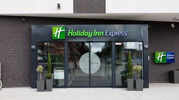 Modernilla designilla varustetun Holiday Inn Express -hotellin ulkoasu: suuri lasinen sisäänkäynti ja ruukuissa olevia kasveja.