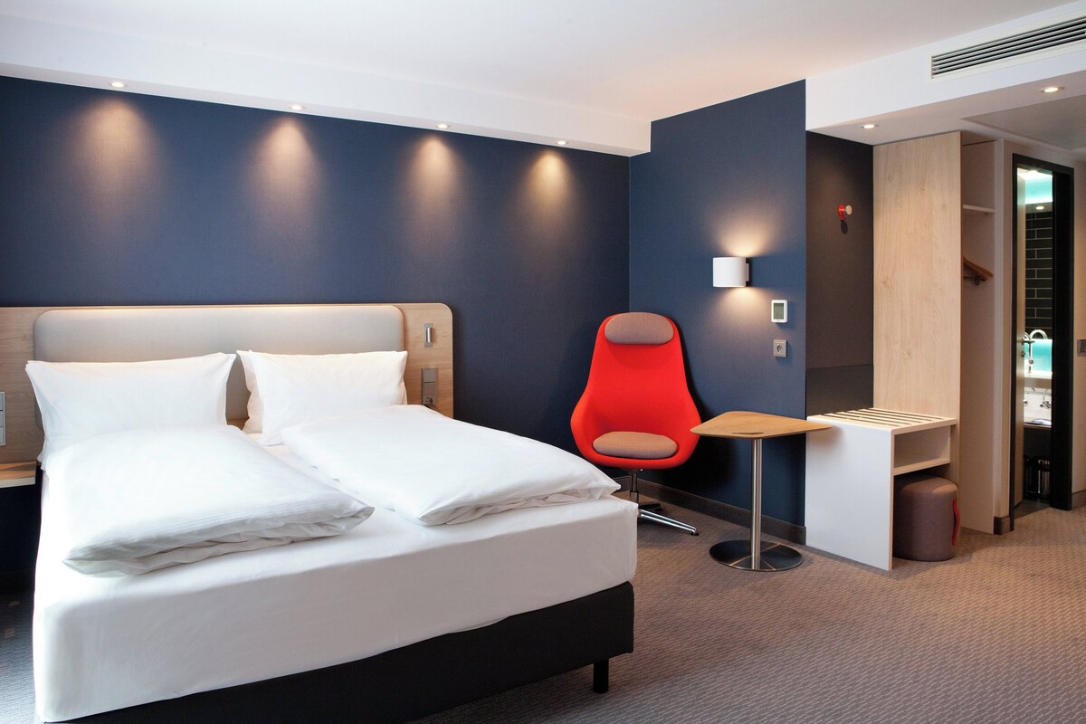 Et moderne hotelværelse med en stor seng, en rød stol og et lille bord.